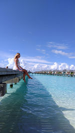 Woman by swimming pool against sea against blue sky