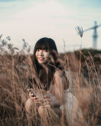 Portrait of smiling young woman on field against sky