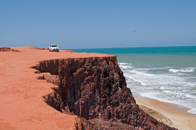 Car on cliff by sea against clear blue sky