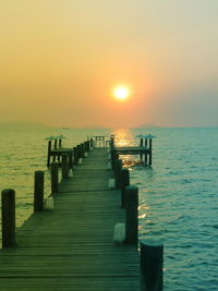 Wooden pier in sea at sunset