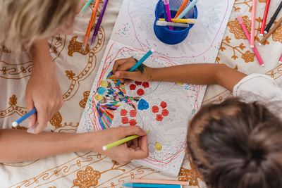 Close-up of the hands of a caucasian mom and hispanic daughter. they are painting while they are lying in the bed.