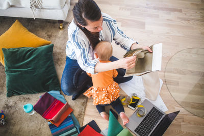 High angle view of daughter playing with busy working mother at home office