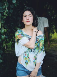 Portrait of beautiful young woman standing against plants in park