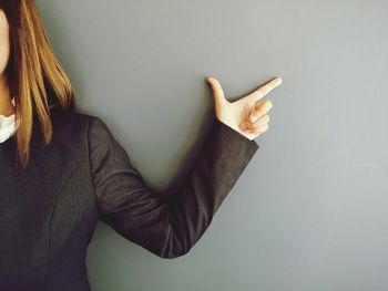 Midsection of woman pointing against gray background