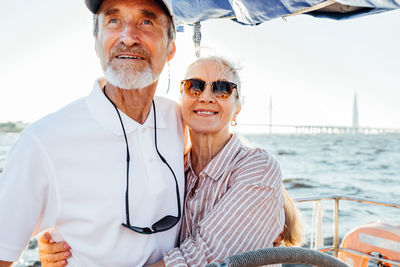 Smiling senior couple embracing while standing in boat at sea