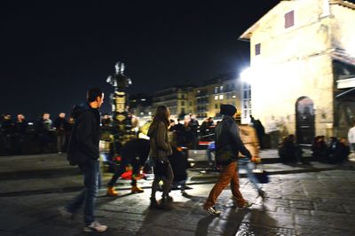 People walking on illuminated street in city at night