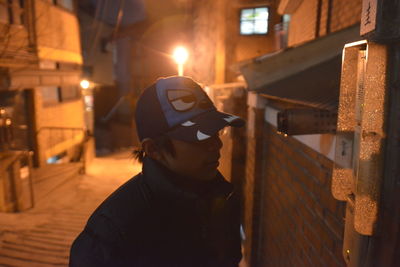 Close-up of man standing by brick wall at night