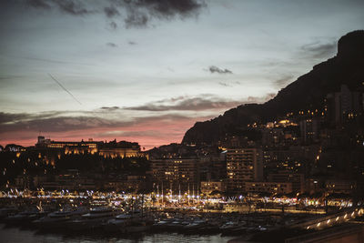 Illuminated buildings by sea against sky at sunset
