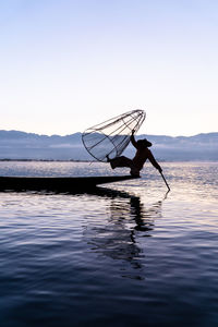 Silhouette of man in boat on inle lake fishing against sky
