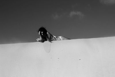 Low angle view of woman lying on retaining wall against sky