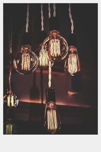 Close-up of illuminated lighting equipment hanging against black background