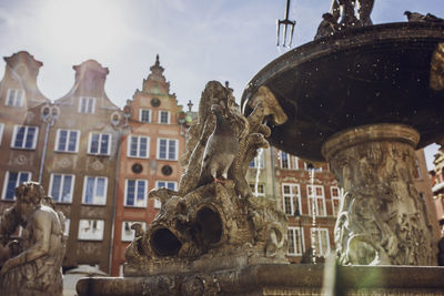 Low angle view of pigeon perching on sculpture at fountain against building