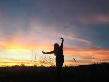 Silhouette woman with arms outstretched standing against sky during sunset