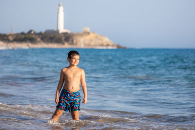 Funny kid enjoying the water of the ocean with a lighthouse background