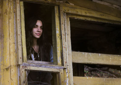 Portrait of beautiful young woman standing against window