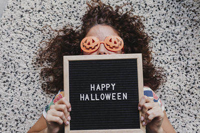 Portrait of woman in novelty glasses holding happy halloween text at home