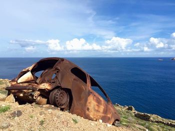 Damaged car by sea against sky