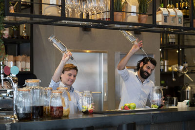 Handsome bartender and trainee pouring alcohol in fruit jar at bar counter