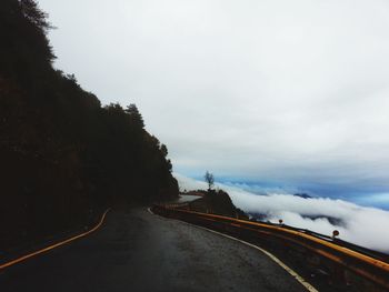 Empty mountain road against cloudy sky