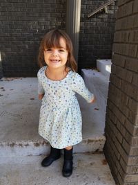 Portrait of a smiling girl standing against brick wall