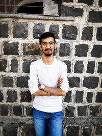 Portrait of young man with arms crossed standing against wall