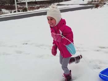 Cheerful girl running with sled on snow covered field