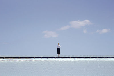 Rear view of woman standing against sky on roof