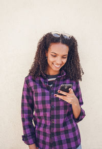 Smiling young woman using mobile phone against wall