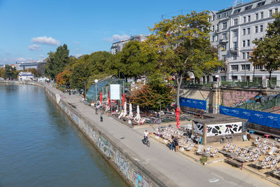 People on canal by buildings in city against sky