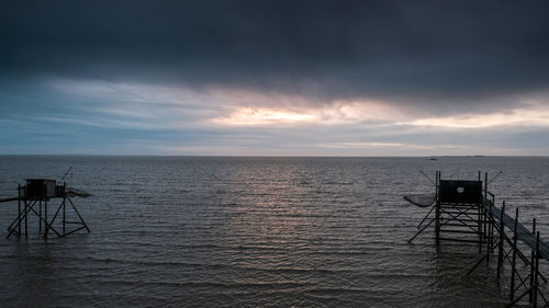 Piers over sea against cloudy sky at dusk