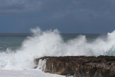 Waves splashing on rocks at shore against sky