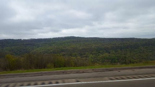 Trees on landscape against cloudy sky