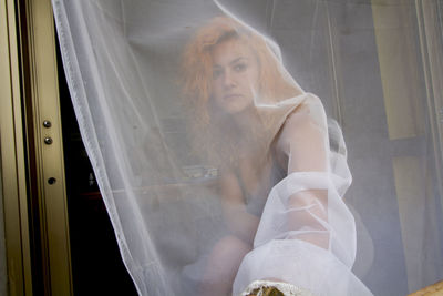 Portrait of woman looking through curtain