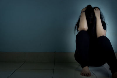 Midsection of woman sitting on floor against wall at home