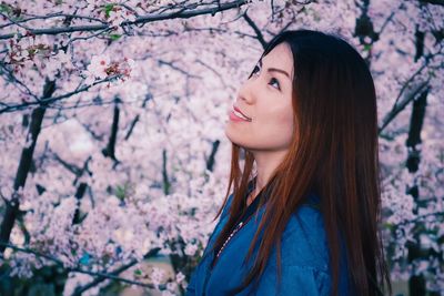 Side view of beautiful woman standing against cherry blossom tree