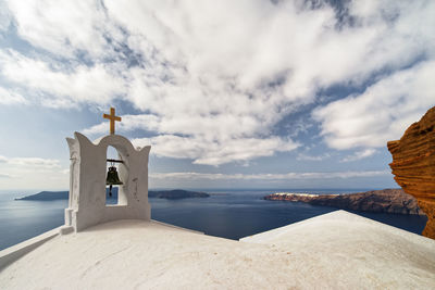 Tower bell by sea against cloudy sky