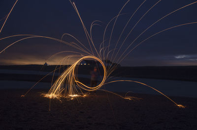 Firework display at beach against sky at night