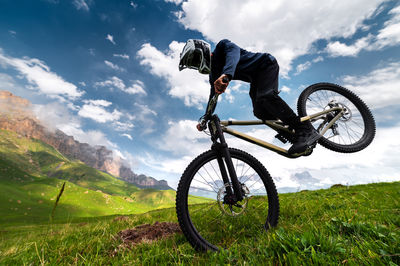Professional man in a full-face helmet performs a front wheelie trick in a field in the mountains in