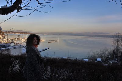 Woman standing by lake against sky during sunset