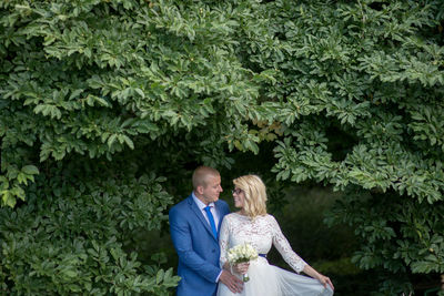 Bridal couple looking at each other while standing amidst tree branches at park