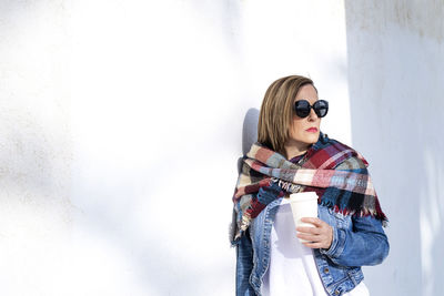 Young woman wearing sunglasses standing against wall