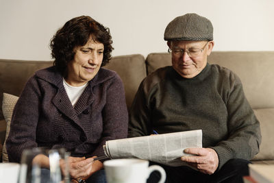 Senior couple reading newspaper while sitting on sofa at home