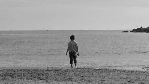 Rear view of boy standing on sea shore against sky