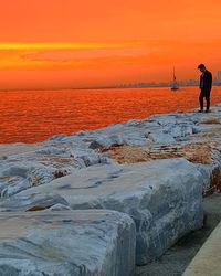 Man standing on beach against orange sky