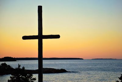 Silhouette cross by sea against sky during sunset