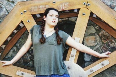 Portrait of woman with braided hair standing against wooden sculpture