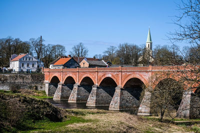 Arch bridge over river by buildings against clear blue sky