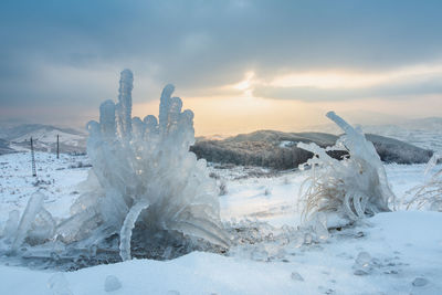 Snow covered land against sky during sunset