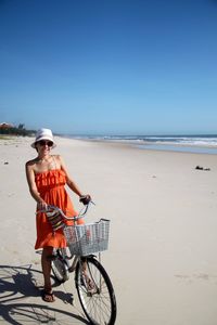 Young woman with bicycle at beach against clear sky during sunny day