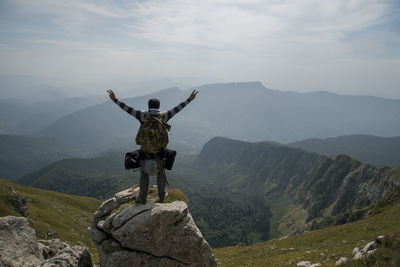 Rear view of male hiker with arms raised standing on cliff against sky